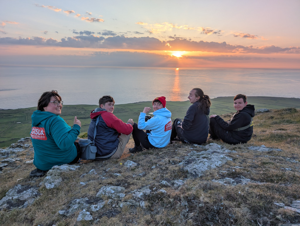 A picture of young people from GISDA watching the sunset from Mynydd Enlli.